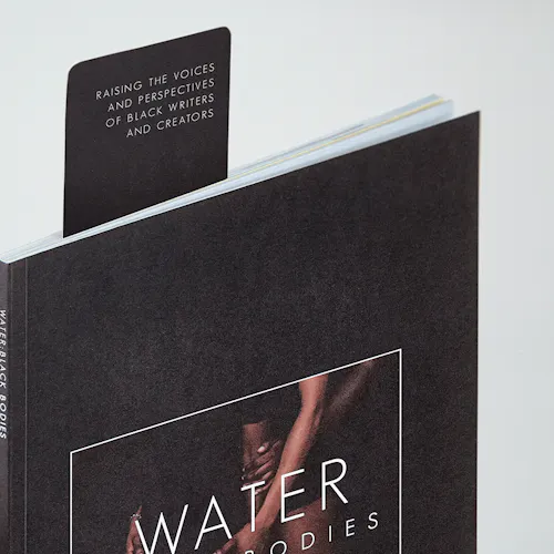 A bookmark sticking out of a literary magazine printed with Water Black Bodies on the black cover.