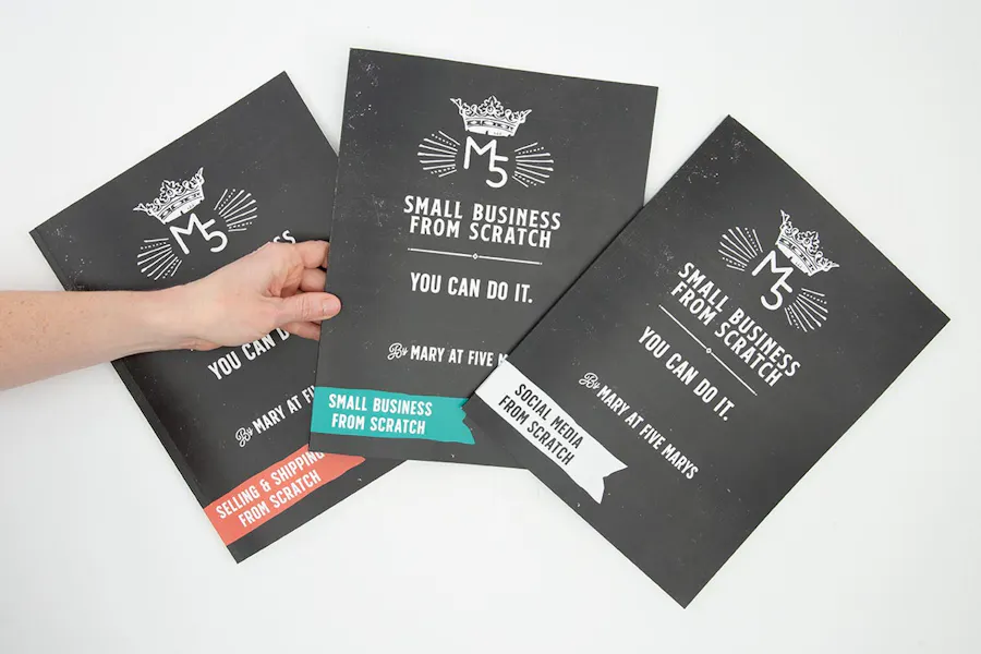 Three marketing manuals printed with black and white covers fanned out with a hand holding the middle one.