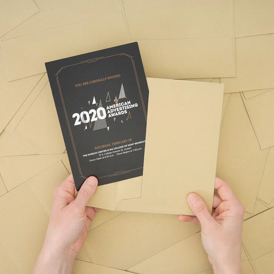 Two hands holding a custom invitation and matching envelope above a pile of scattered envelopes.