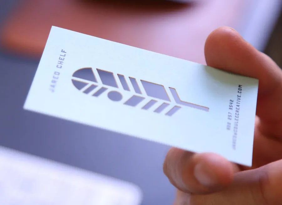 A hand holding a die-cut business card with a leaf design.