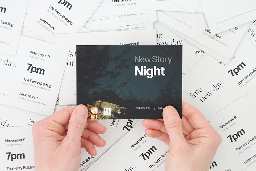 Two hands holding a custom invite printed with New Story Night on the front above scattered invitations below.
