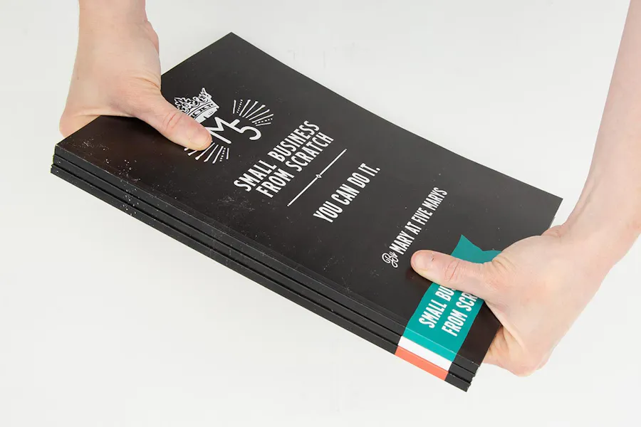 Two hands holding a stack of three custom marketing booklets with perfect bindings and black covers.