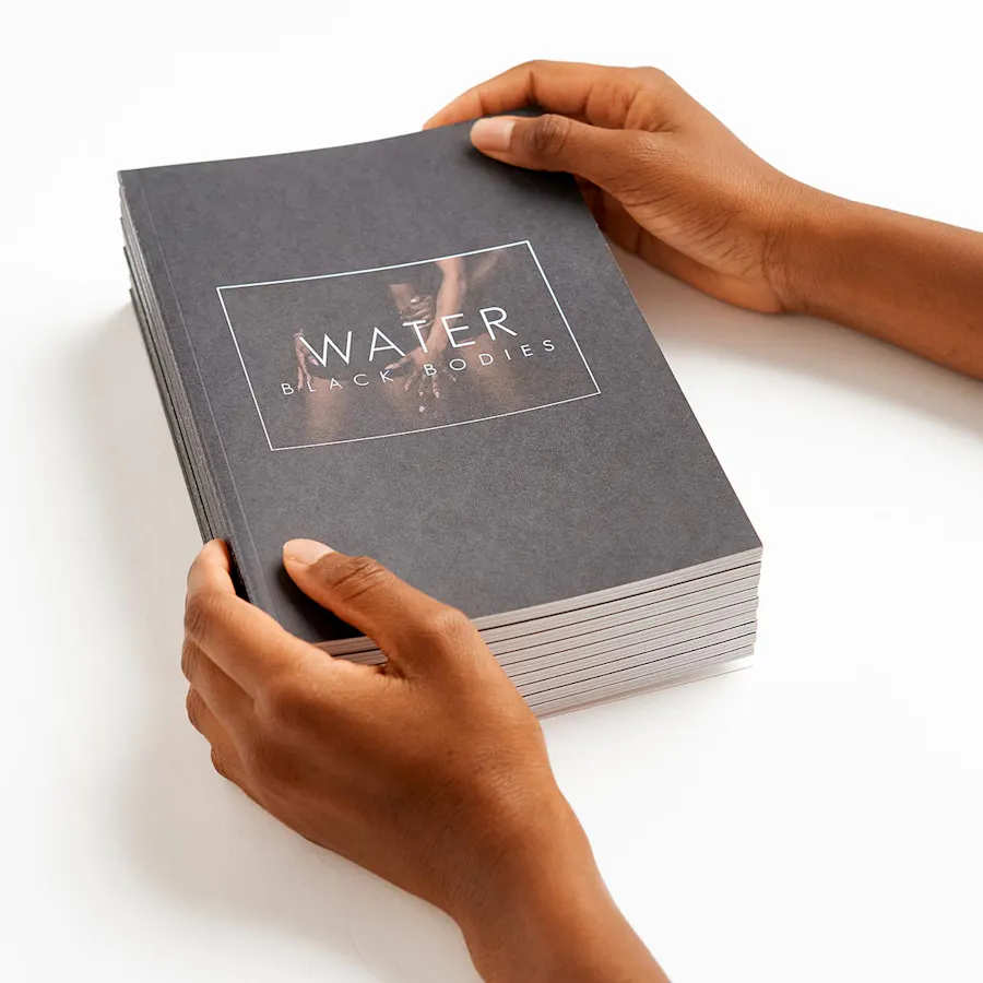 Two hands holding a stack of literary magazines printed with a black cover and Water in white letters.