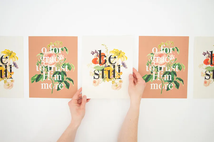 Five custom posters printed with devotional sayings lined up in a row with two hands holding the poster in the middle.