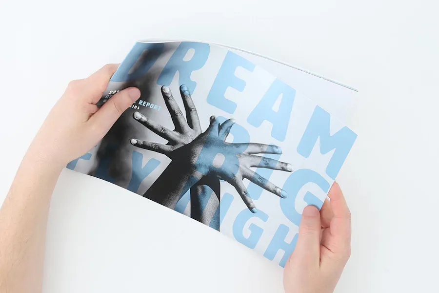 Two hands holding a nonprofit advertising booklet with Dream Big Fly High in blue on the front.