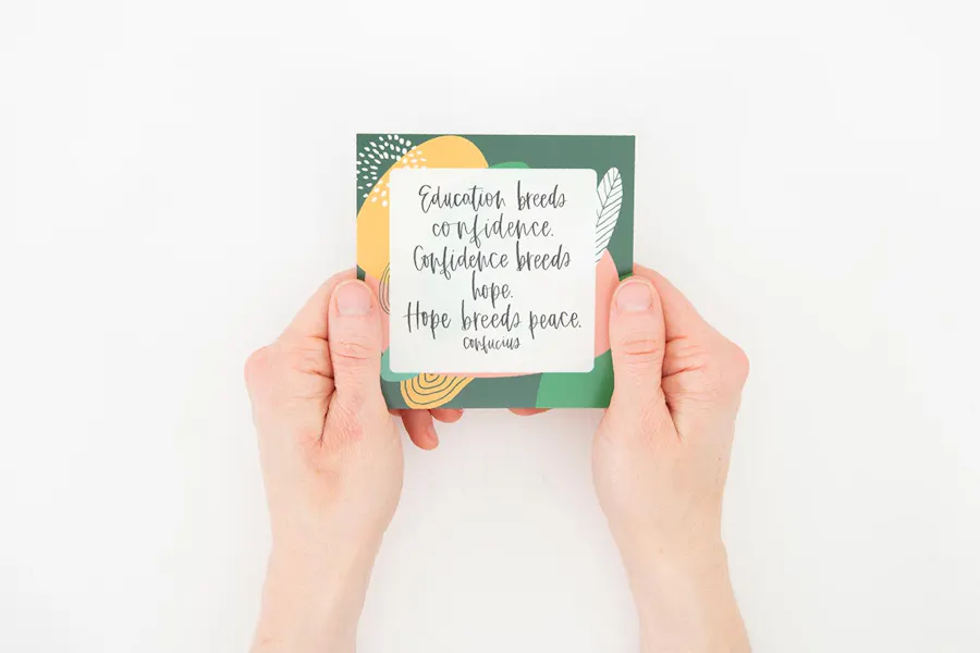 Two hands holding a motivational flashcard with a quote from Confucius in black letters.