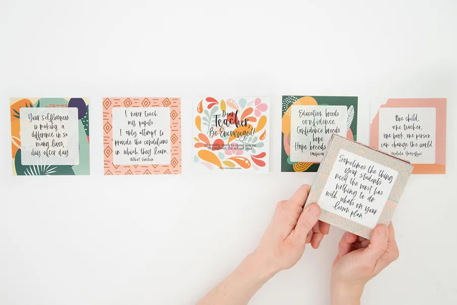 Five cards with motivational sayings for teachers lined up in a row with two hands holding another card above them.