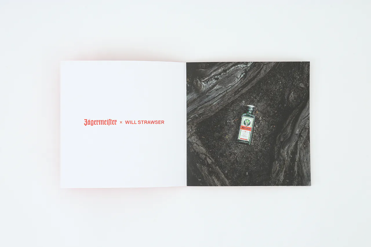 A photography book laying open to Jagermeister x Will Strawser in red and an image of a small bottle of alcohol on the ground.