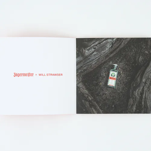 A photography book laying open to Jagermeister x Will Strawser in red and an image of a small bottle of alcohol on the ground.