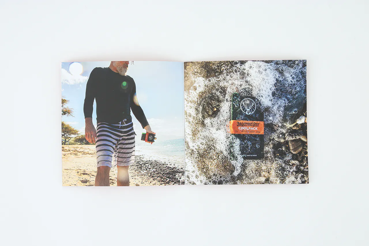 A photography portfolio laying open to a man in shorts on the beach and a bottle of alcohol laying in water on rocks.
