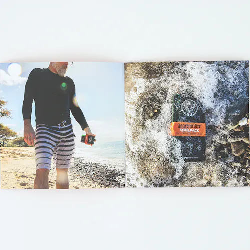 A photography portfolio laying open to a man in shorts on the beach and a bottle of alcohol laying in water on rocks.