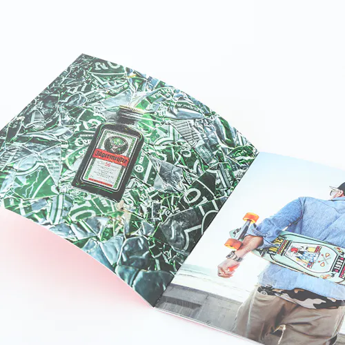 A photography lookbook laying open to images of a bottle of alcohol and a person holding a skateboard behind their back.