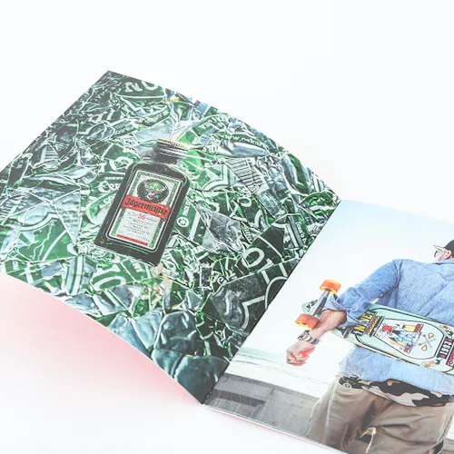 ©Will Strawser A photography lookbook laying open to images of a bottle of alcohol and a person holding a skateboard behind their back.