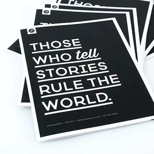 ©Adam Ryan Morris A stack of fanned-out photography booklets printed with a black cover and Those Who Tell Stories Rule the World in white.