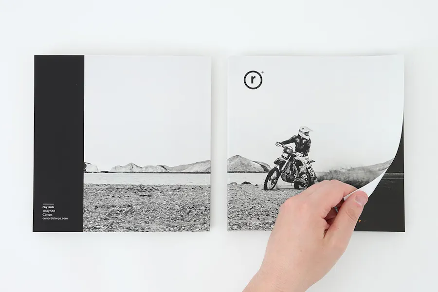 A hand turning the page of a custom portfolio booklet printed with black and white imagery.