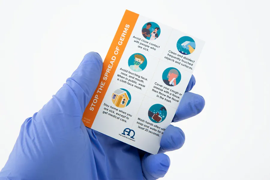 A gloved hand holding a custom business card printed with health and safety information.