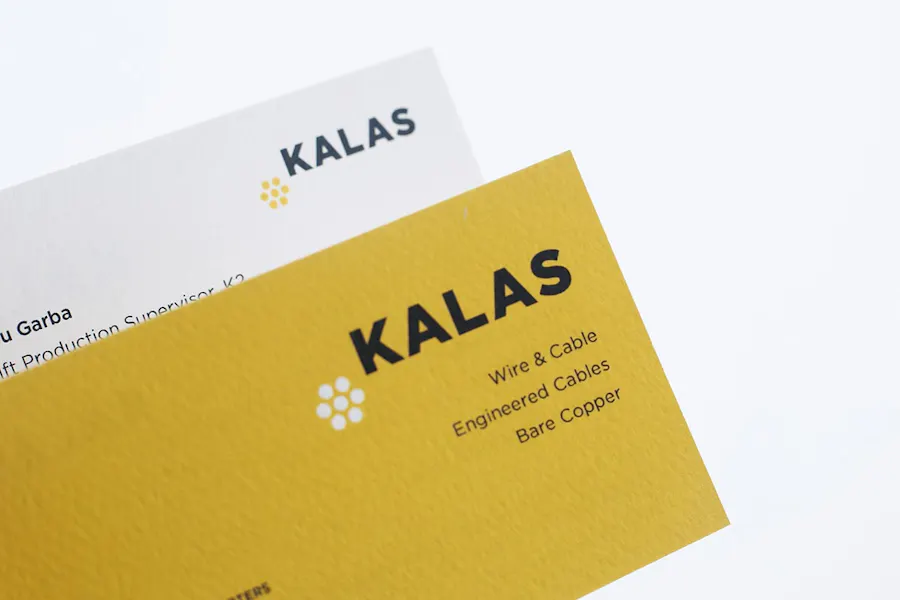 A custom business card with a yellow design and Kalas in black text overlapping another card with a white design.