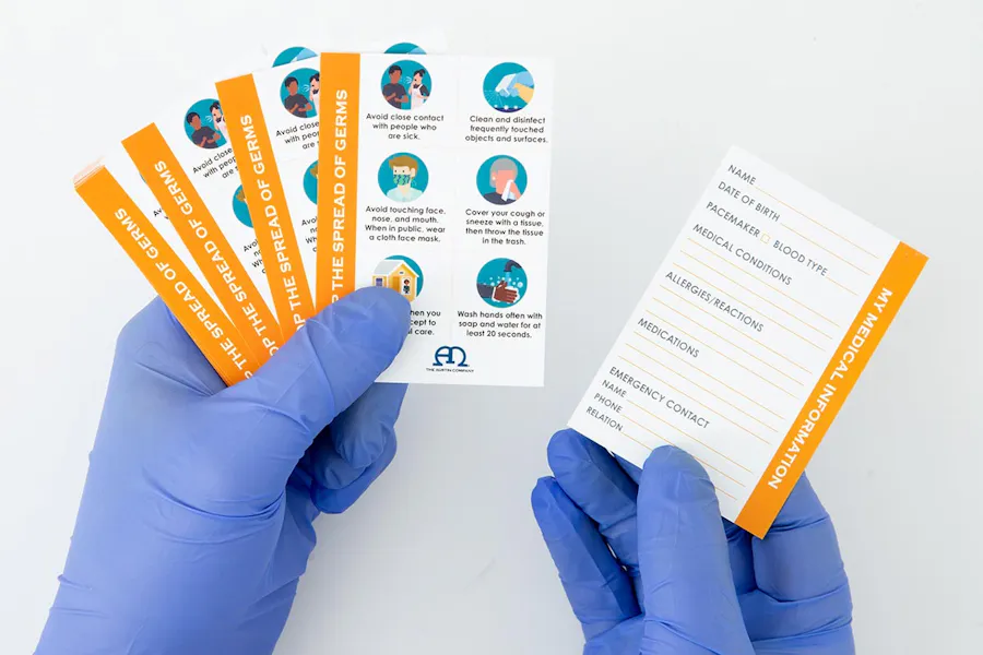 Two gloved hands holding custom business cards printed with health and safety information.