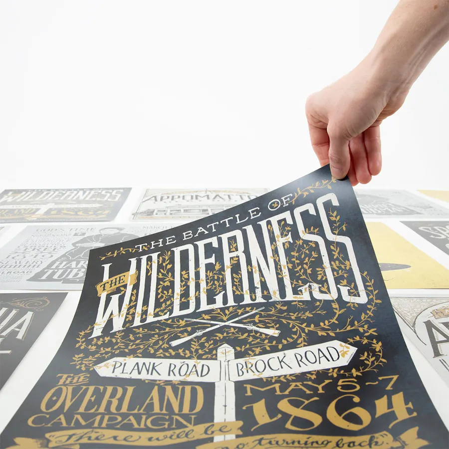 A hand holding the corner of a poster with The Battle of the Wilderness in white text.