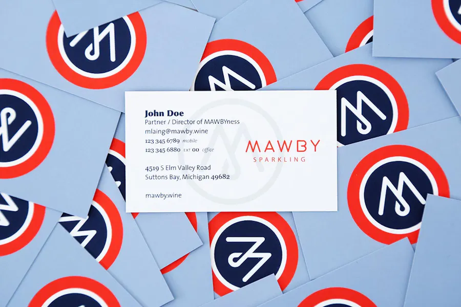 A custom business card with contact info on the front laying on top of a pile of scattered business cards.