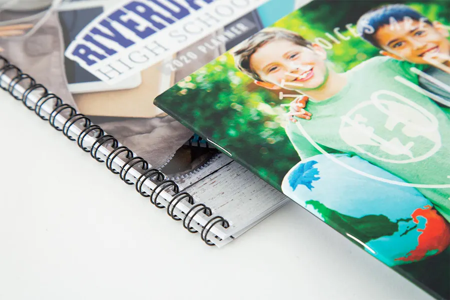 A school planner printed with a wire coil binding and a school marketing booklet with smiling kids on the cover.