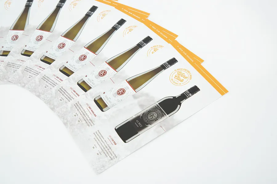 Wine club flyers fanned out in a row with images of two wine bottles and a gold strip along the top.