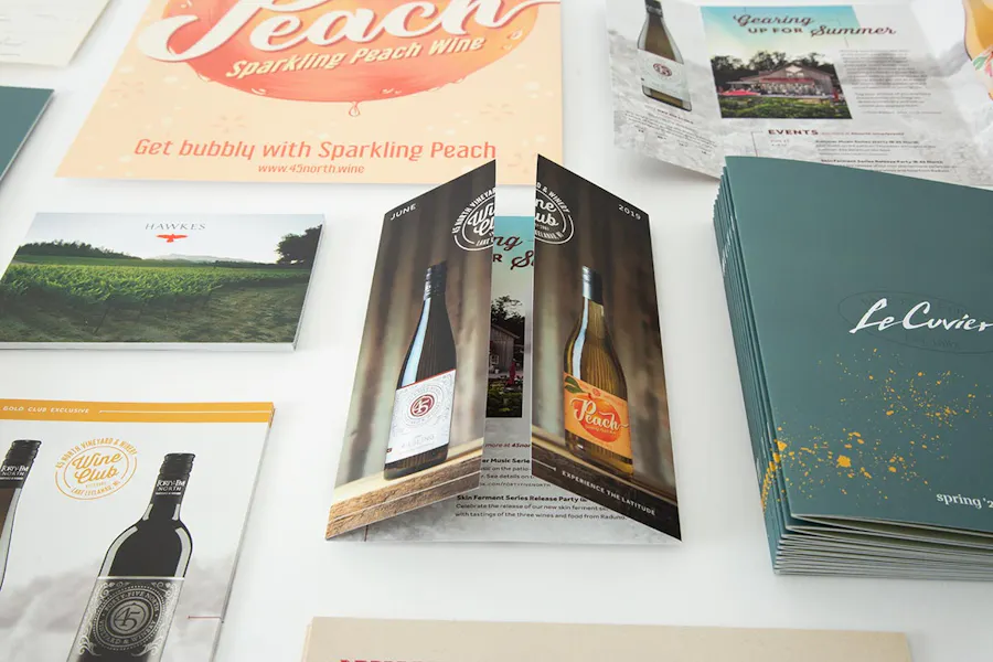 Winery print marketing materials laid out in rows, including a brochure, menus, posters and flyers.