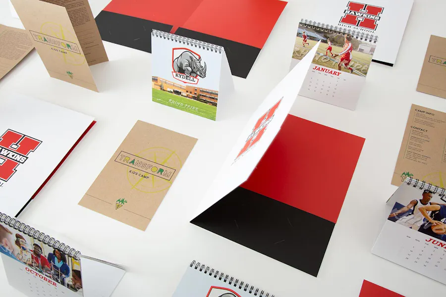 Custom print materials for schools, including red, white and black pocket folders, desk calendars and flyers.