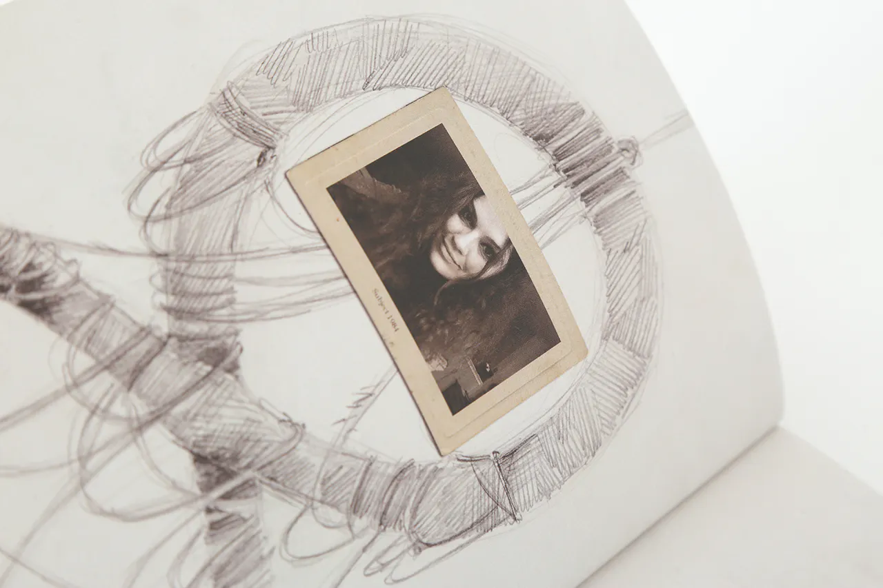 A black and white sketch of a round hanging frame with a sepia-colored picture of a woman in the middle.