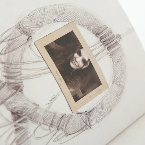 A black and white sketch of a round hanging frame with a sepia-colored picture of a woman in the middle.