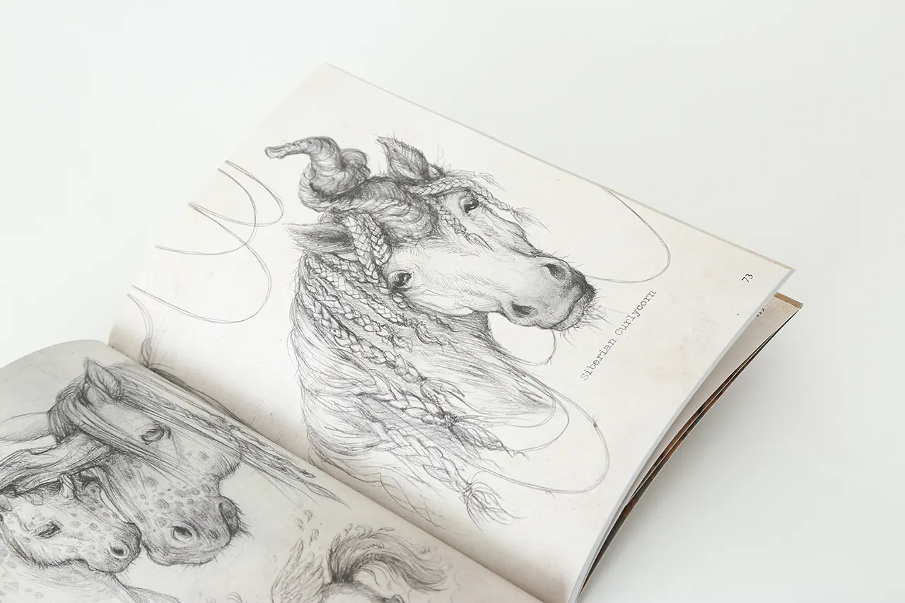 A sketchbook laying open to black and white illustrations of a horse with braided hair.