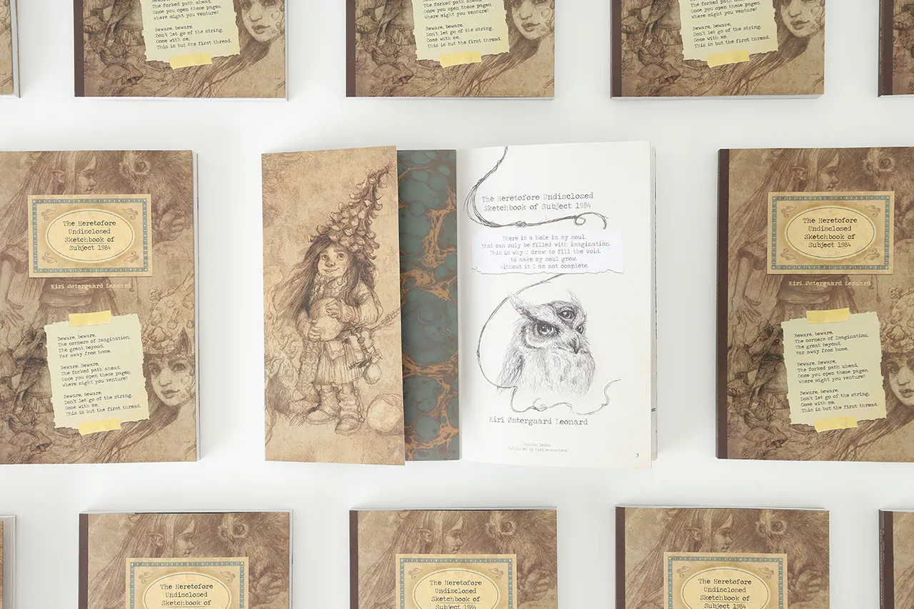 A custom sketchbook laying open to illustrations of a young girl wearing a hat and a three-eyed bird.