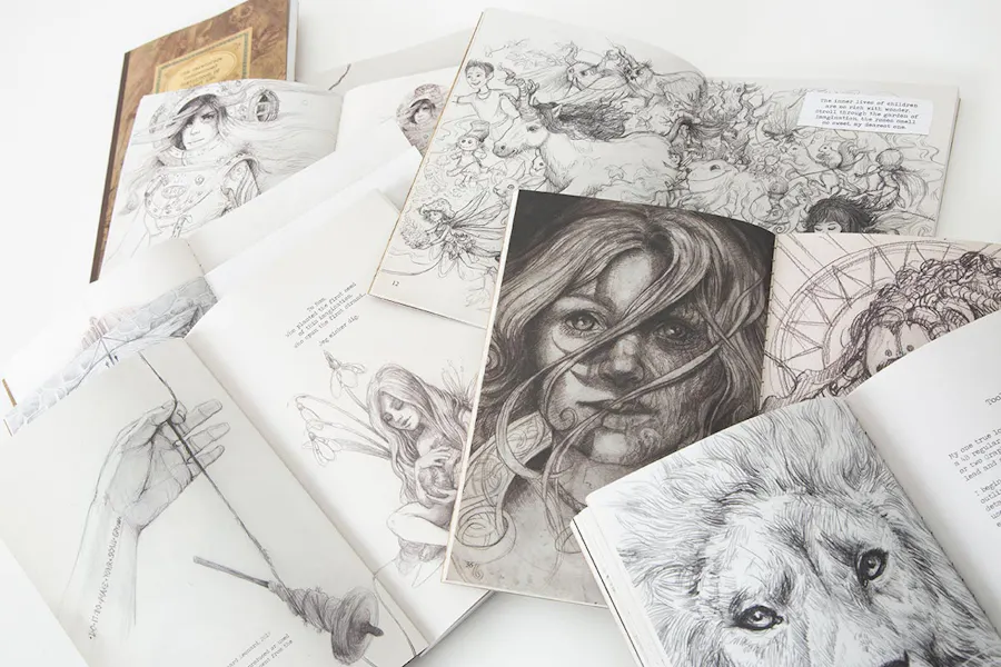 A pile of booklets laying open to black and white illustrations and fantasy artwork.