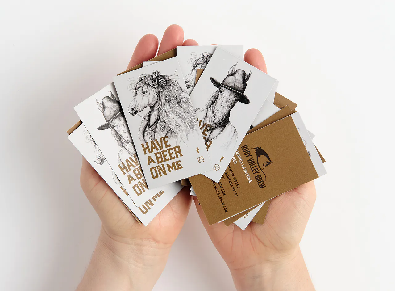 Two hands holding fanned-out business cards printed with Ruby Valley Brew, horse graphics and Have a Beer on Me.
