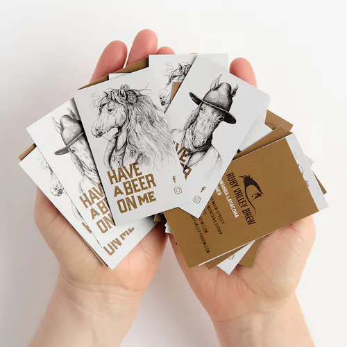 0028_2020-08-SP-Ruby-Valley-Brew-Horse Two hands holding fanned-out business cards printed with Ruby Valley Brew, horse graphics and Have a Beer on Me.