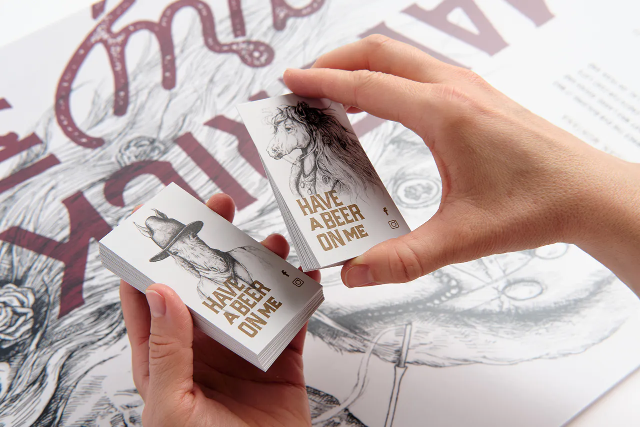 Two hands holding business cards printed as beer cards with a horse graphic and Have a Beer on Me.