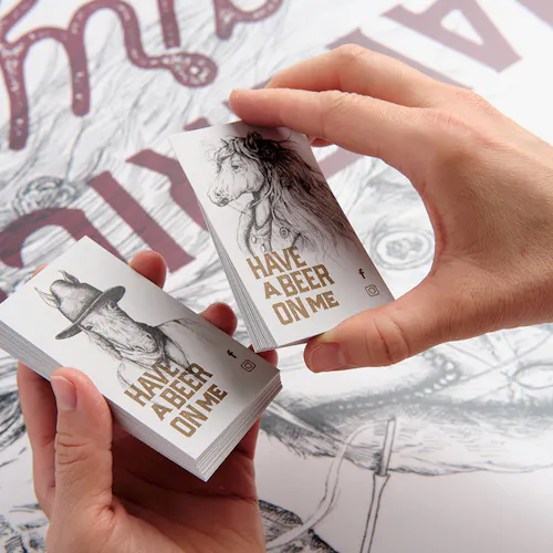 Two hands holding business cards printed as beer cards with a horse graphic and Have a Beer on Me.