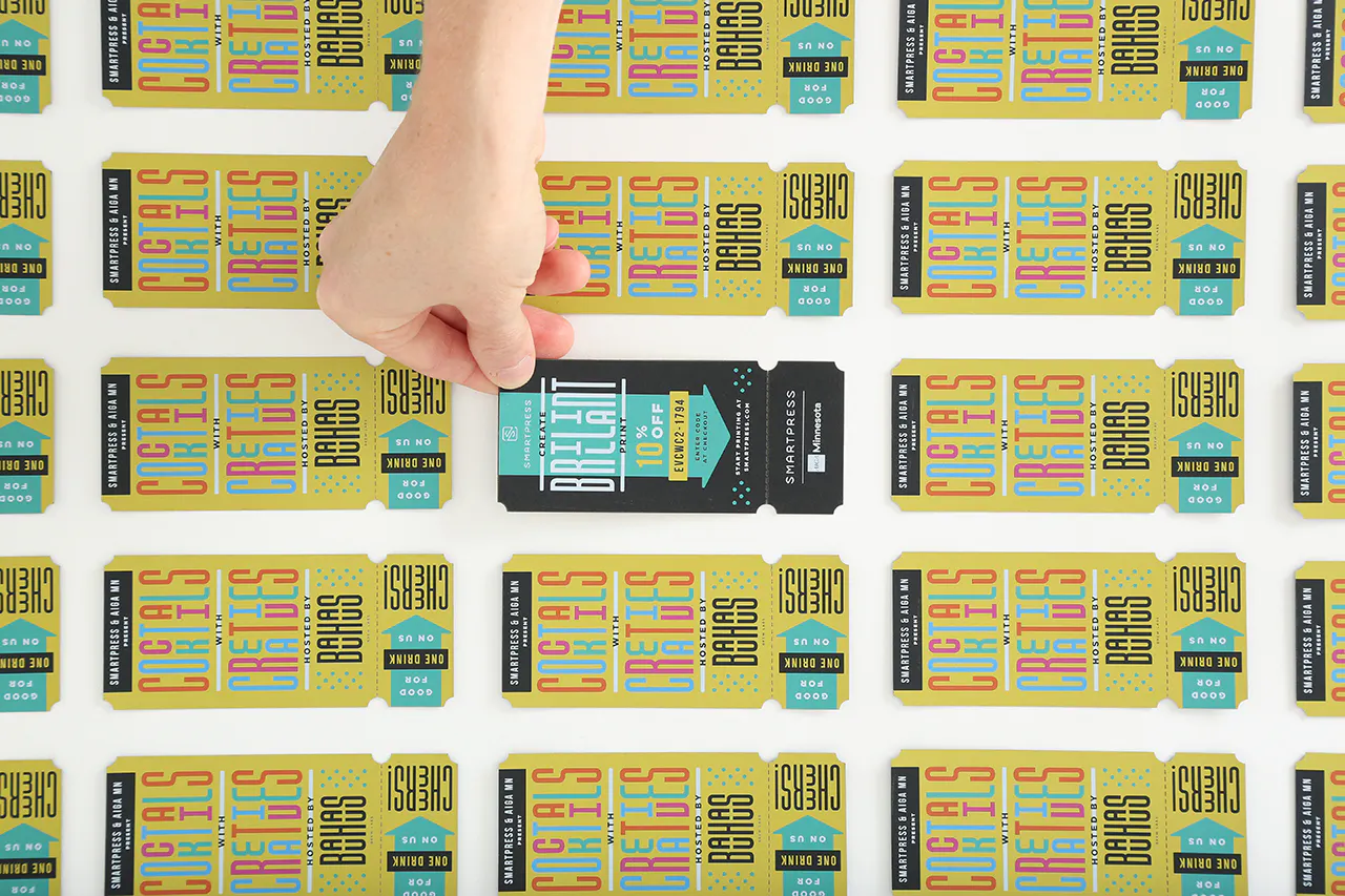 A hands holding the corner of a custom printed drink ticket in black and teal with more yellow tickets around it.