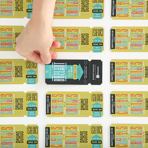 A hands holding the corner of a custom printed drink ticket in black and teal with more yellow tickets around it.