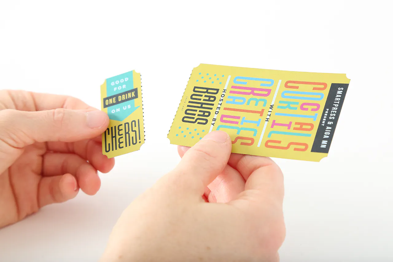 Two hands holding a custom drink tickets printed with Cocktails with Creatives in black, teal, pink and yellow.