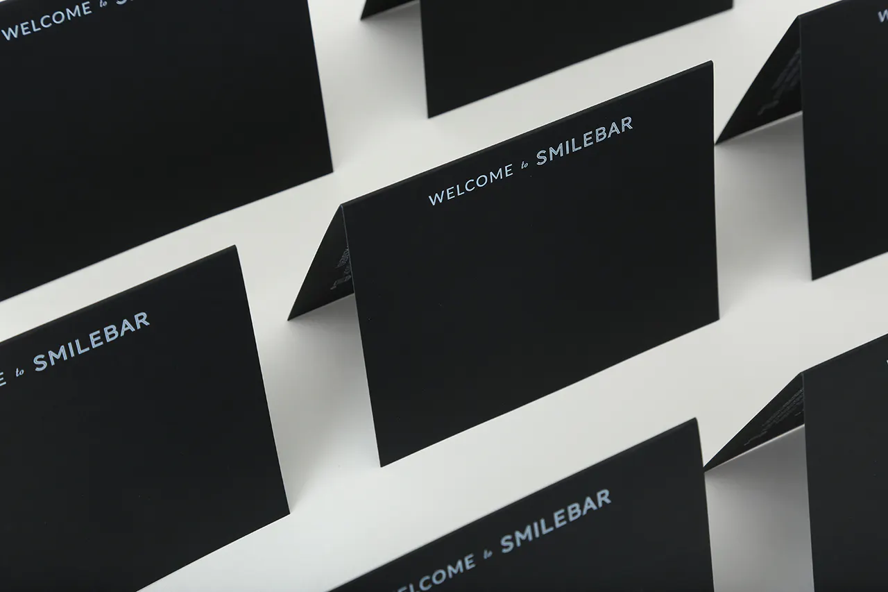 Custom cards lined up in rows printed on black paper stock with Welcome to Smilebar in white ink.