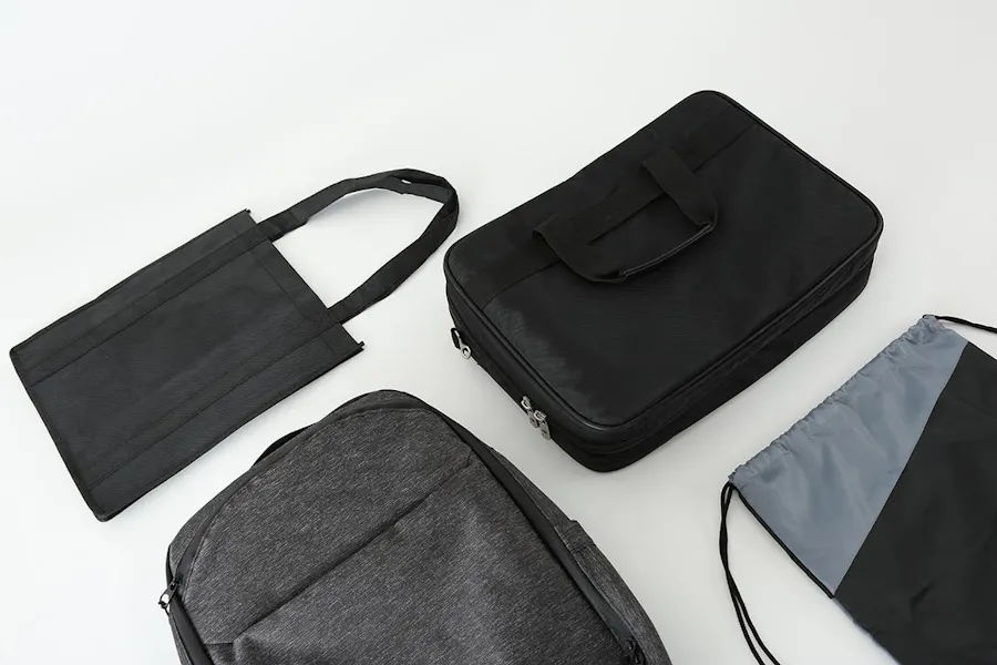 A black tote bag, black computer bag, dark gray backpack and a black and gray drawstring bag laying next to each other.
