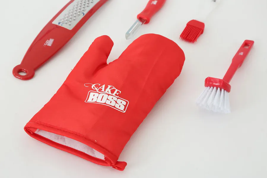 A red oven mitt branded with Cake Boss and a red grater, peeler and two brushes.