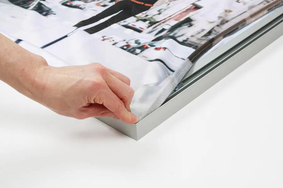 A hand putting the corner of an SEG graphic into its aluminum frame.