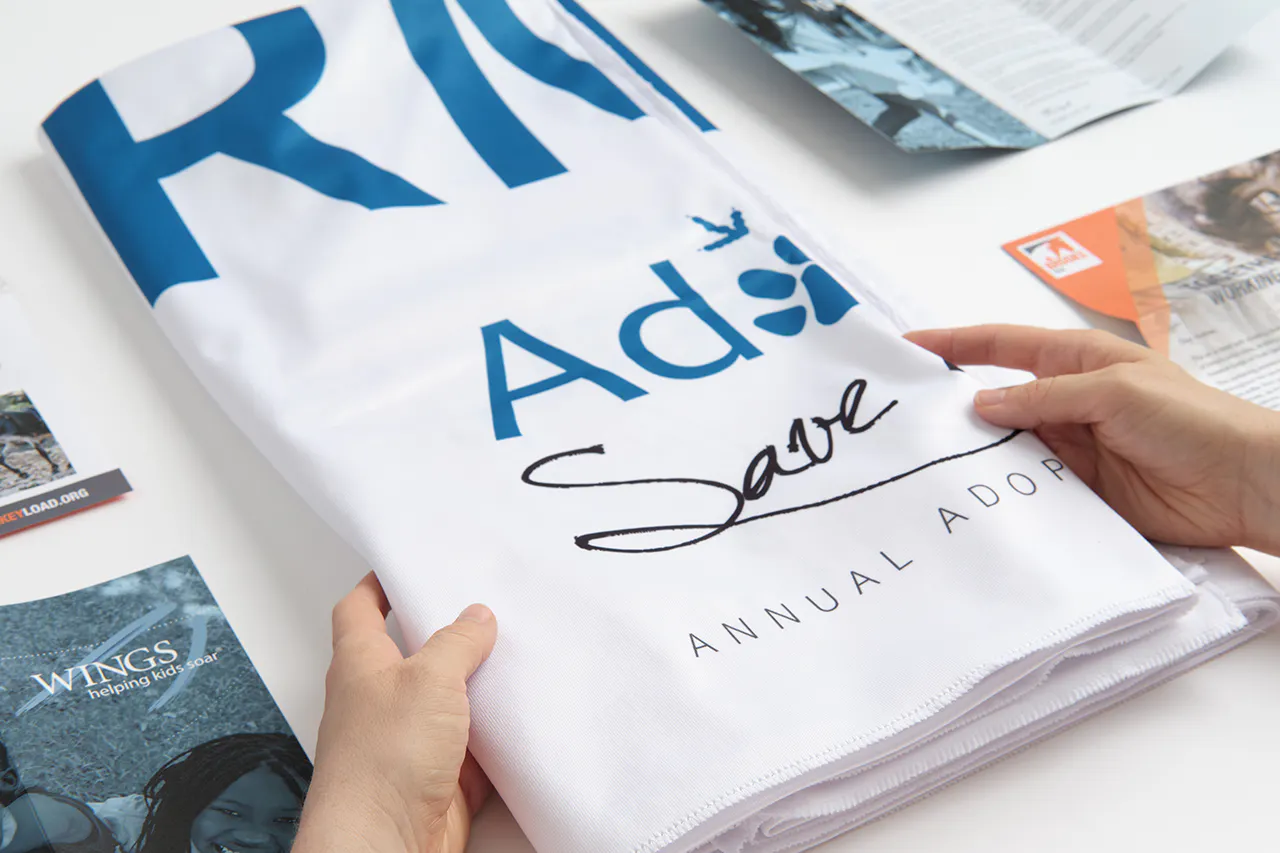 Two hands holding a folded table throw printed with a white background and Annual Adopt in black text.