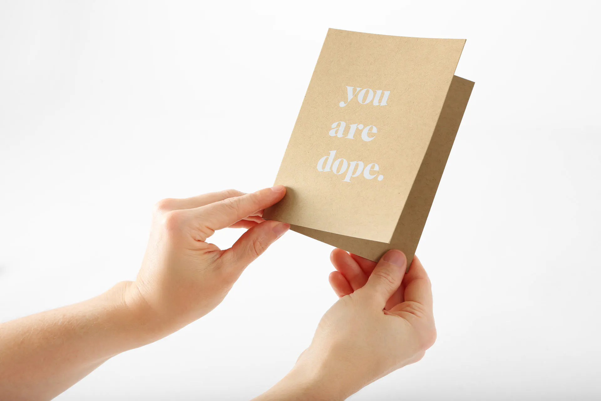 Two hands holding a custom card printed on Kraft paper with you are dope. in white ink on the front.