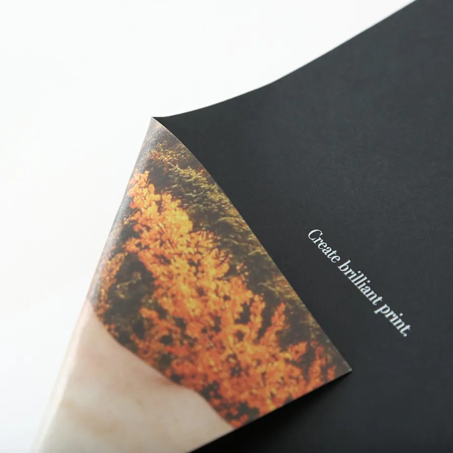 Black paper stock printed with Create brilliant print. in white ink on the front and its bottom corner folded back.