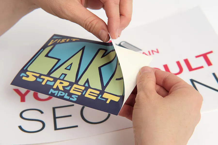 Two hands peeling a decal printed with Lake Street off its backing with another larger decal underneath it.