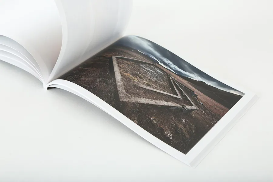 A photography portfolio booklet laying open to an image of a barren field and the outline of a cement structure.