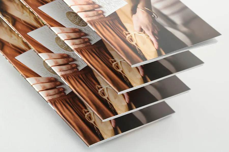 A stack of four tiered catalogs printed with a saddle stitch binding and a woman holding a card on the cover.